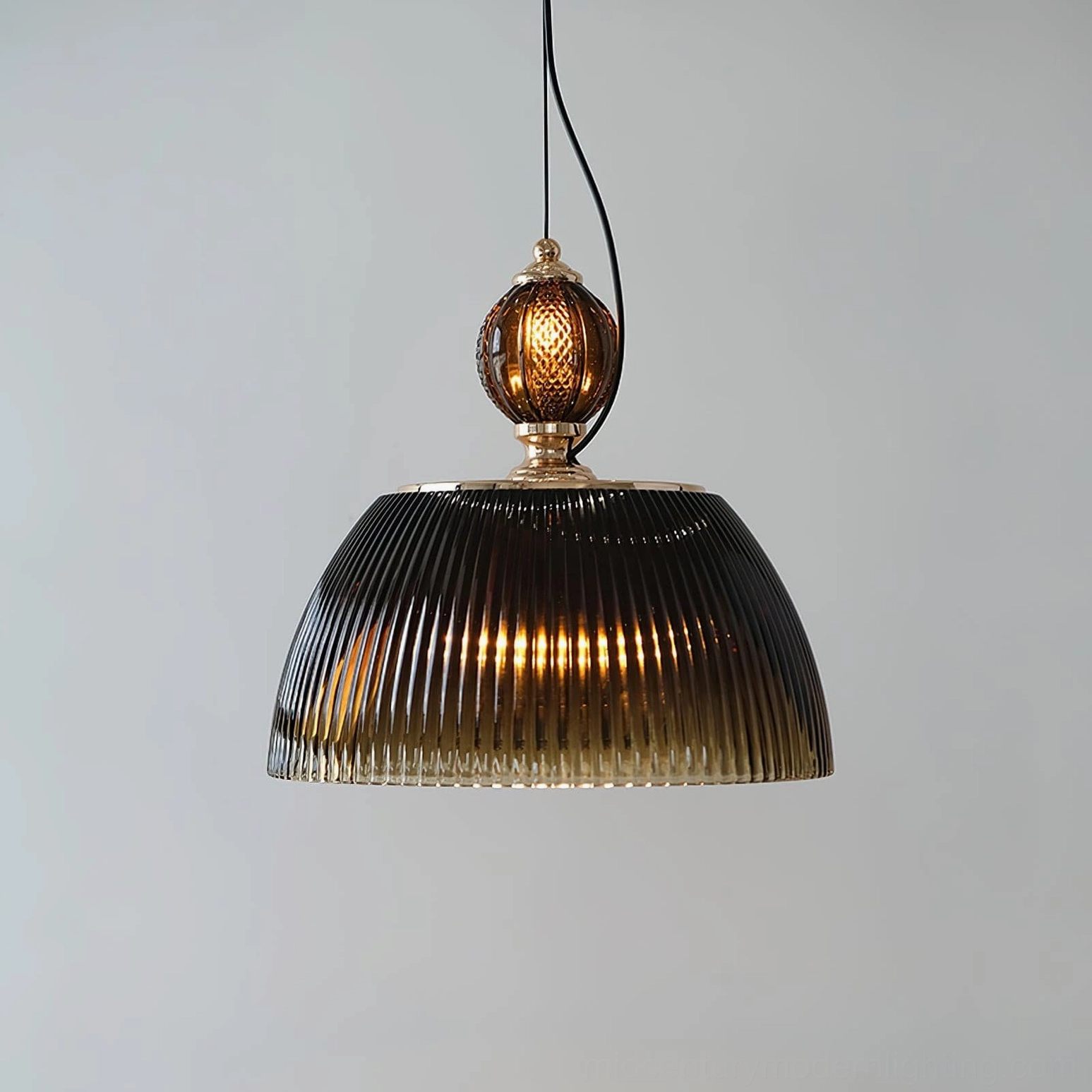 Low angle frontal view of ribbed pendant shade with brass hardware and dark smoky glass against light background