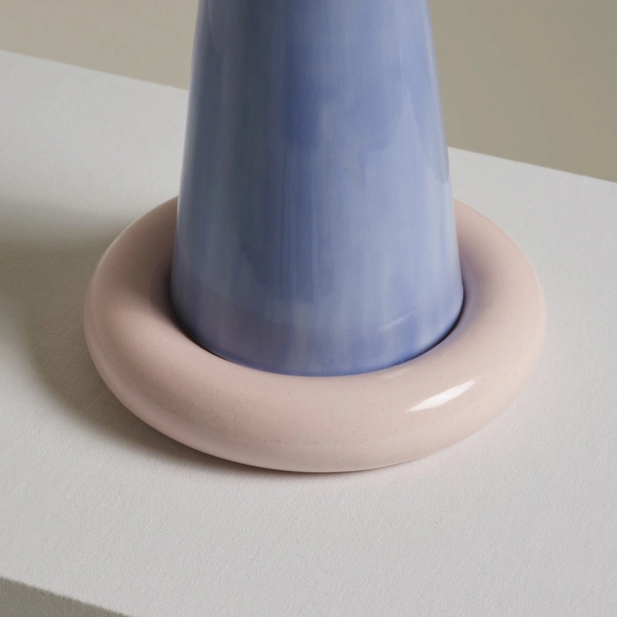 Overhead top-down close-up of blue ceramic lamp base and pink circular ring foot on white surface