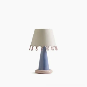 Ribbon table lamp full frontal view with blue ceramic base, pink circular foot, and off-white fabric shade with pink scalloped trim on white studio backdrop