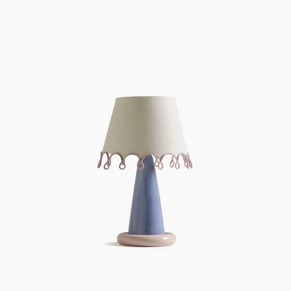 Ribbon table lamp full frontal view with blue ceramic base, pink circular foot, and off-white fabric shade with pink scalloped trim on white studio backdrop