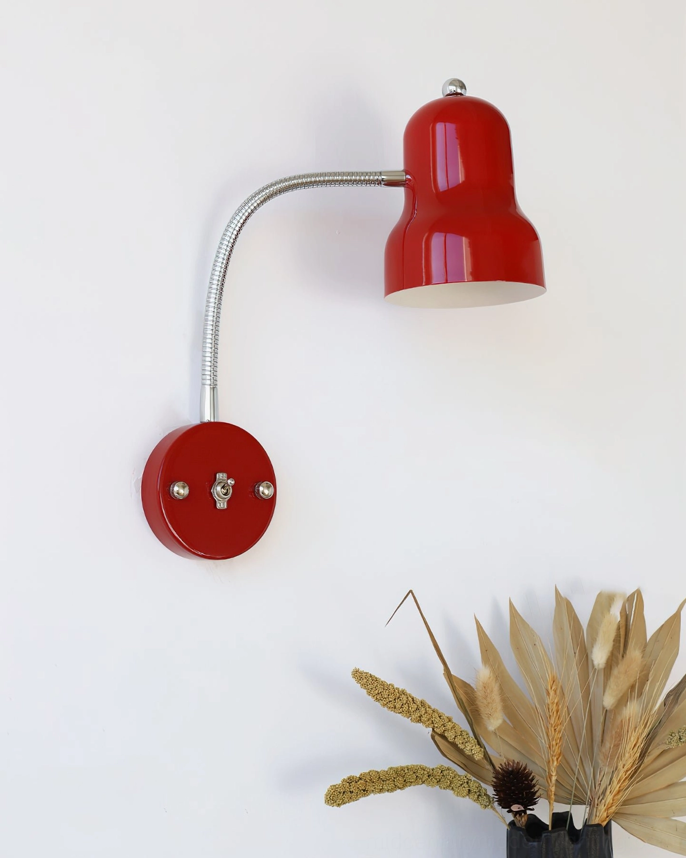 Minimalist red wall lamp with straight silver gooseneck and round chrome base, side view with dried wheat