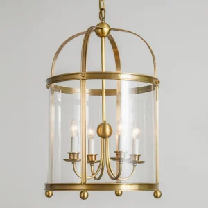 Close-up detail of Rieka pendant showing brushed brass frame, four candle-style light sockets, and transparent glass enclosure