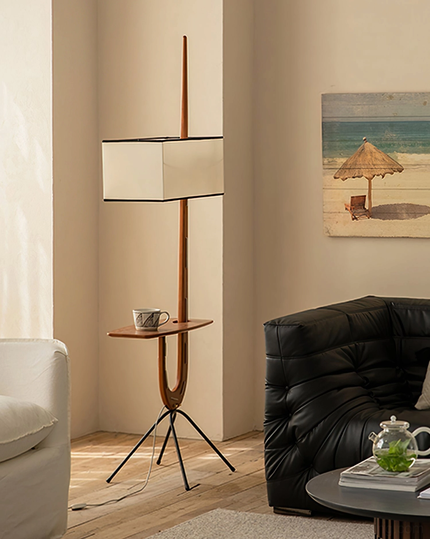 Rispal Giraffe Floor Lamp beside black leather sofa with decorative wall art, teapot and books on console shelf, three-quarter styling view