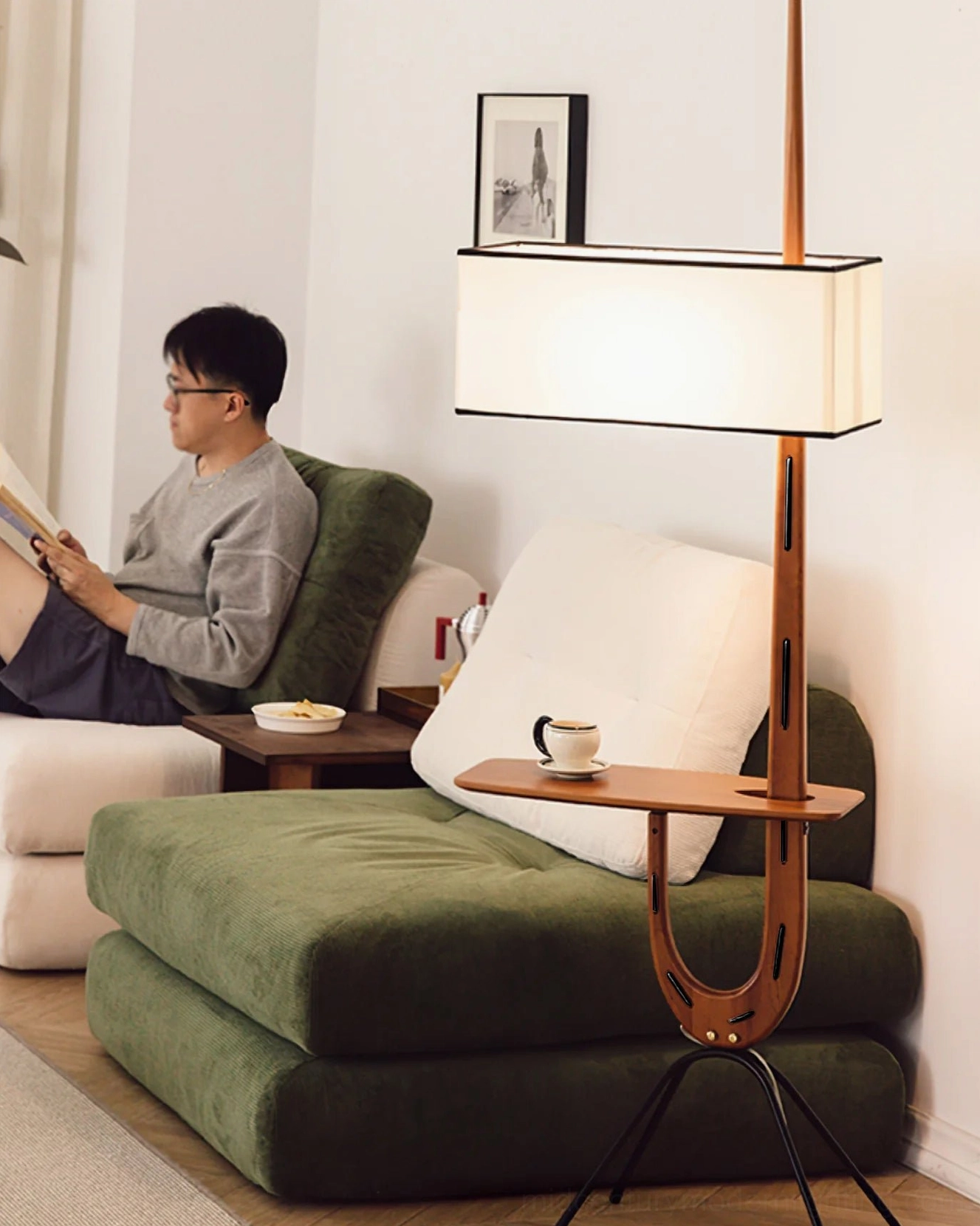 Man reading by Rispal Giraffe Floor Lamp beside green couch, warm reading light casting over seated area, cozy home setting