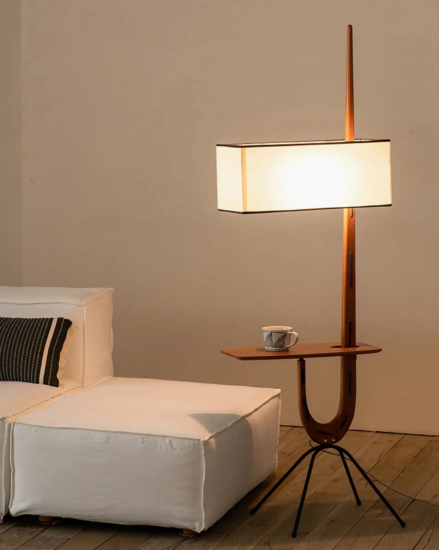 Illuminated Rispal Giraffe Floor Lamp casting warm diffused light over white modular sofa, side angle view of lit shade