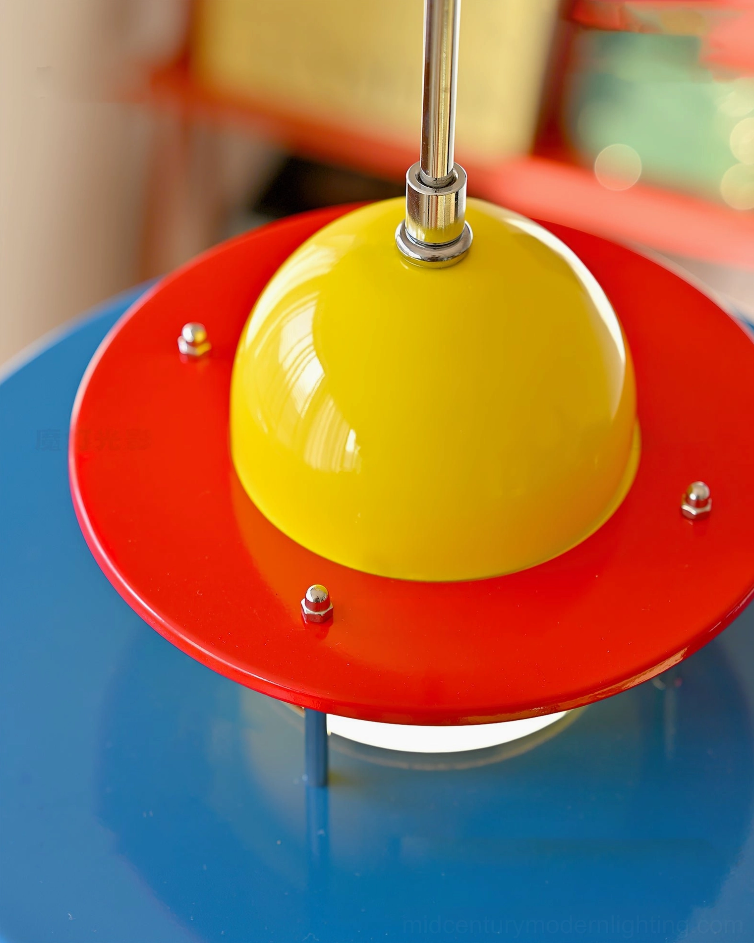 Rolly pendant top section close-up featuring glossy yellow dome and red metal disc layers with blue tabletop background