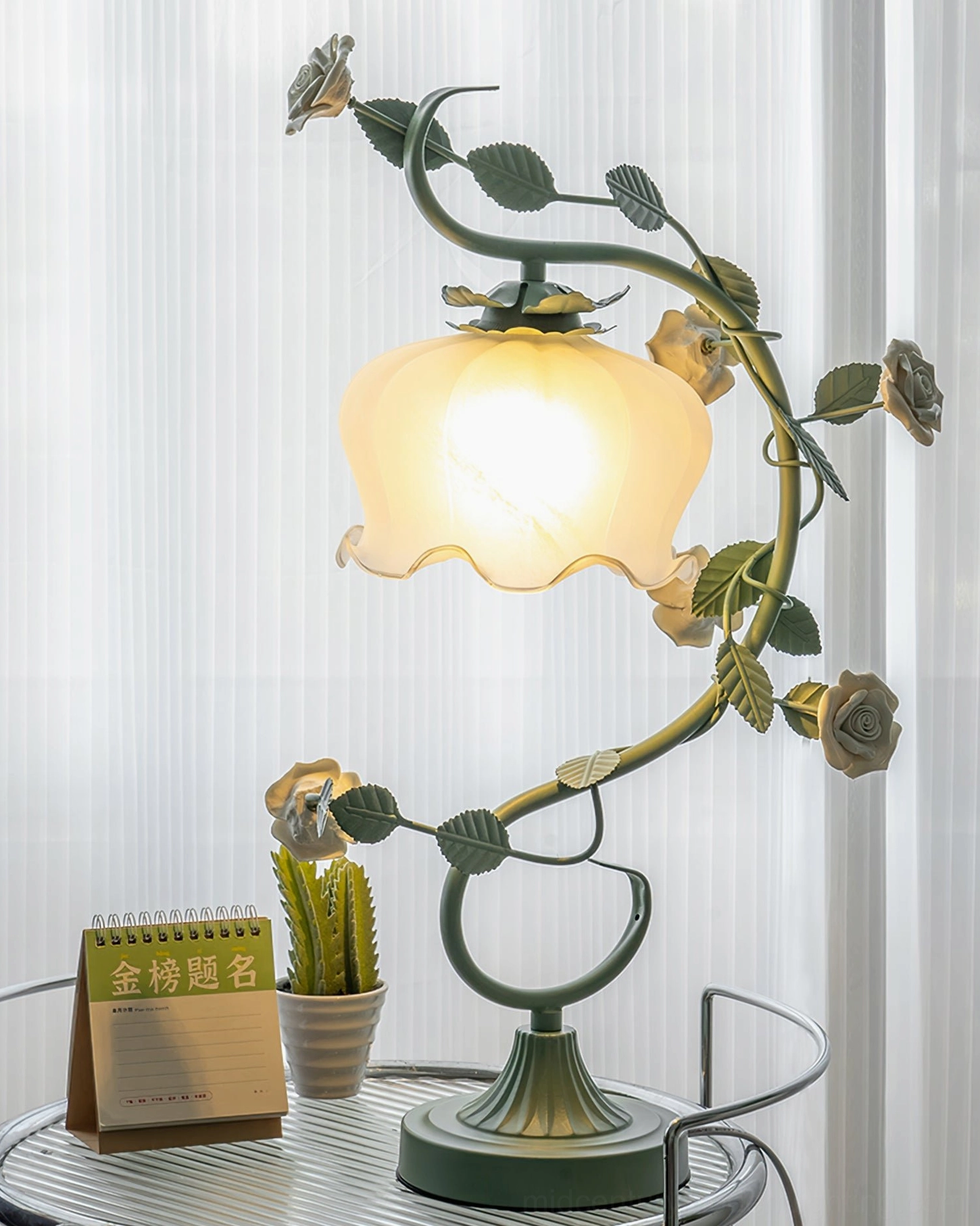 Rose vine table lamp illuminated on small round table with calendar and potted cactus, glowing lampshade