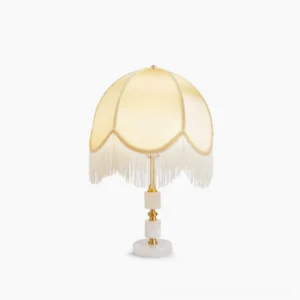 Roussillon brass and marble table lamp with cream fabric shade and white tassel fringe, front view studio shot