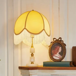 Lit Roussillon table lamp with yellow scalloped shade and brass trim on vintage shelf, warm ambient lighting