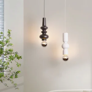 Two Rudd pendant lights in black and white cylindrical design hanging in modern bedroom with potted plant