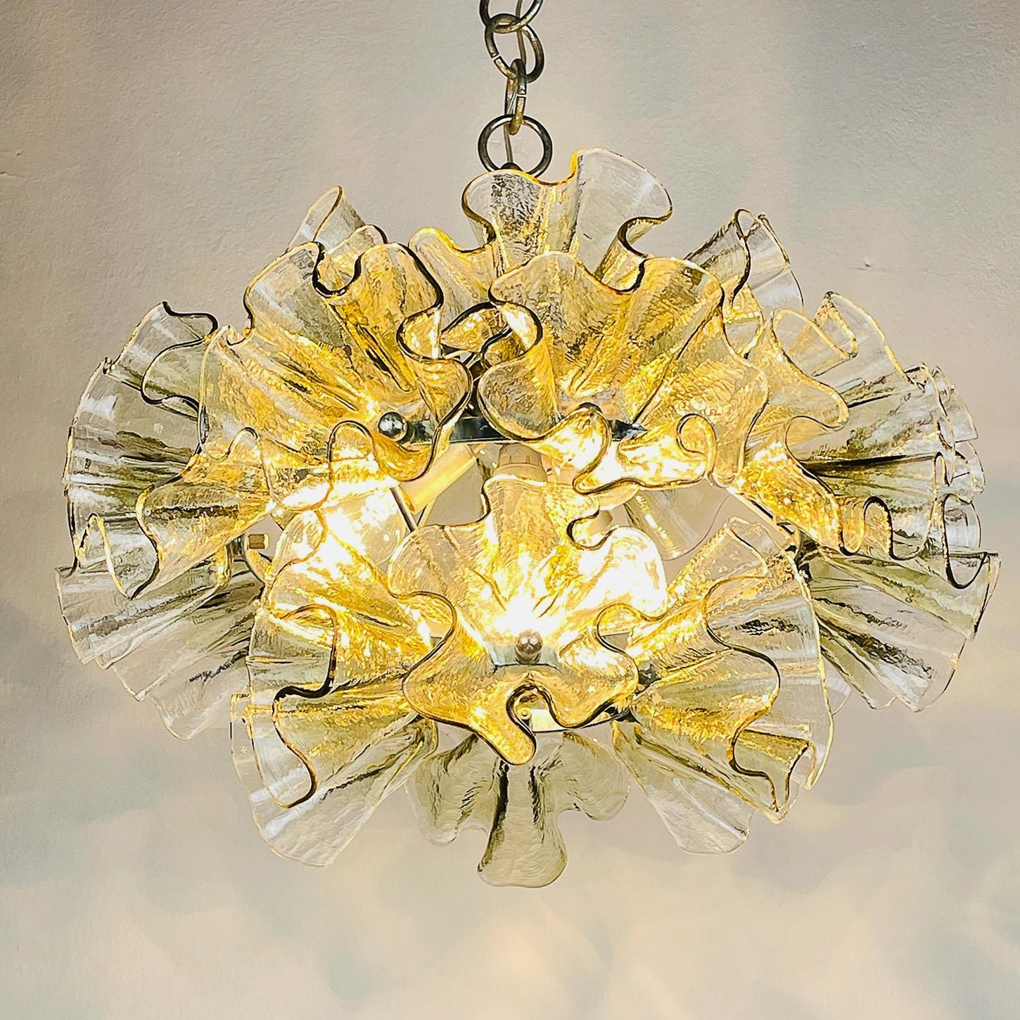 Illuminated ruffled petal glass chandelier with warm amber light glowing through clear and green tinted glass