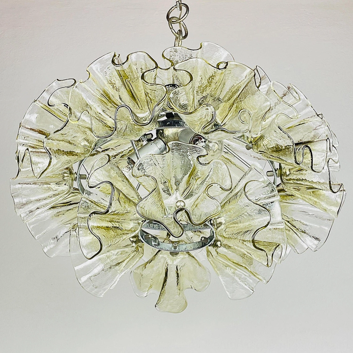Three-quarter side view of ruffled petal glass pendant with exposed central chrome fixture and layered glass petals