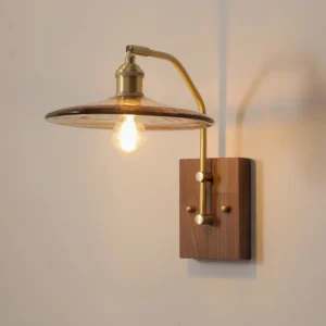 Close-up detail of Runia wall lamp showing curved brass arm and exposed Edison bulb filament against warm neutral wall