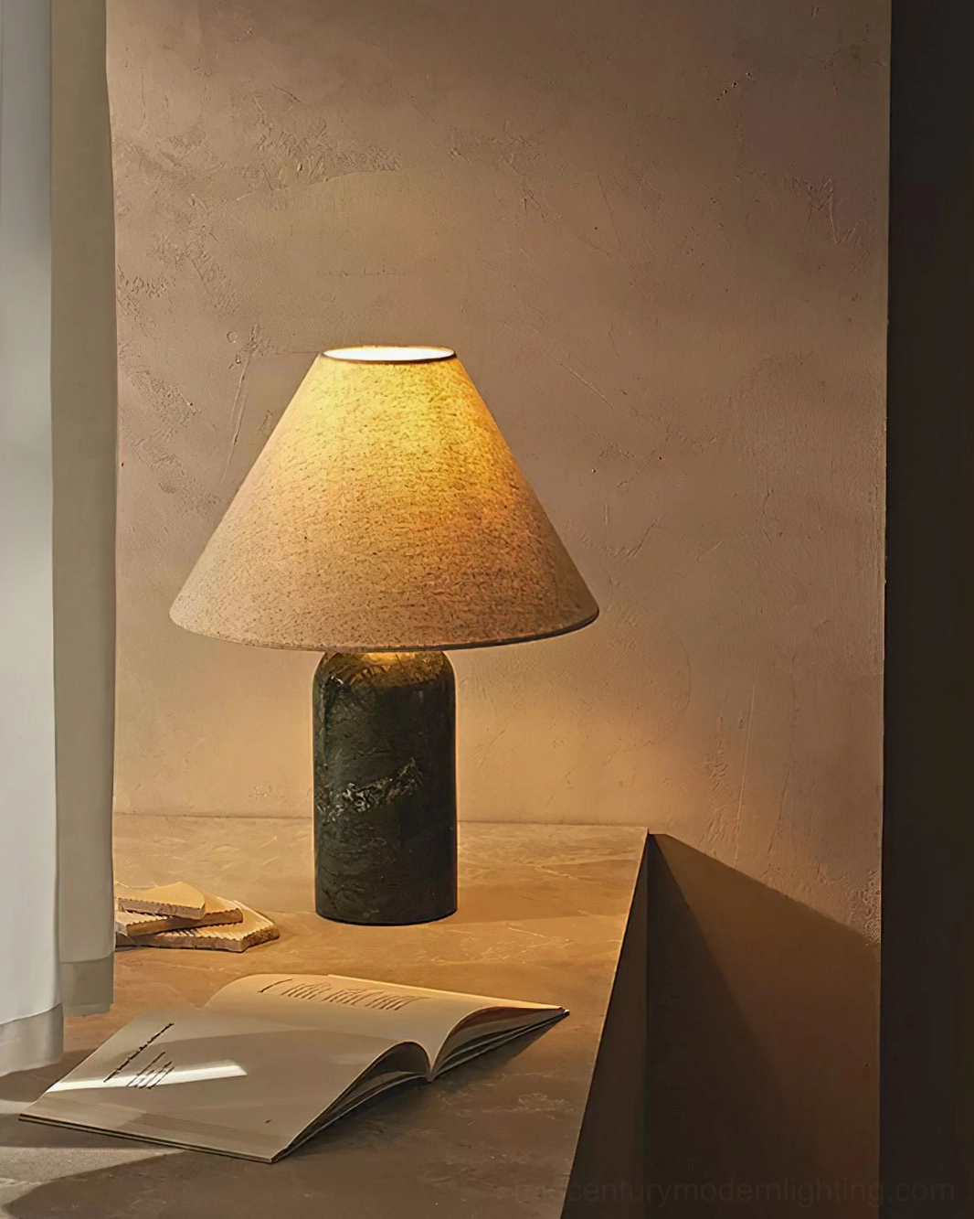 Dark green marble table lamp with tan linen shade in cozy home corner nook, open book on table, warm glowing ambient light