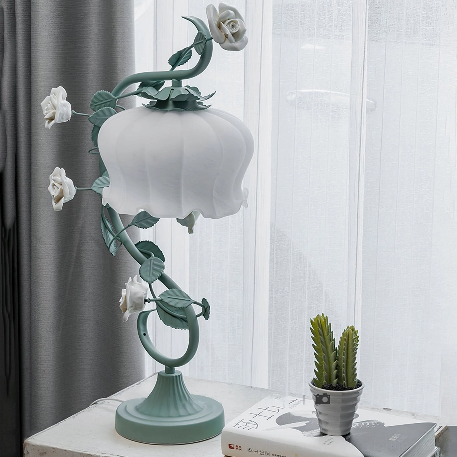 Sage green rose vine table lamp with white ruffled shade in soft interior lighting, styling perspective