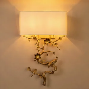 Sanremo wall sconce illuminated on residential wall creating warm ambient light through fabric shade, ornate brass base with botanical bird motif