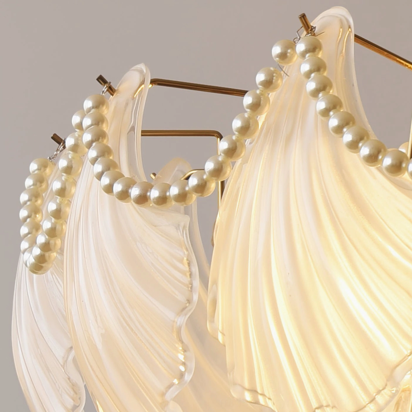 Close-up macro detail of scallop shell chandelier showing faux pearl trim, layered glass texture and warm glow