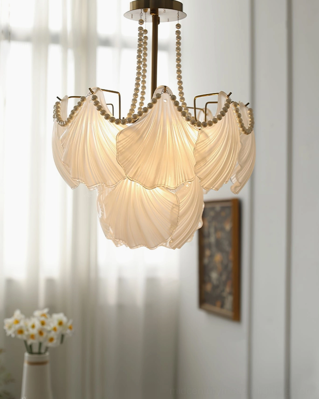 Three-quarter side angle view of glass shell chandelier with pearl trim accents and brass hardware