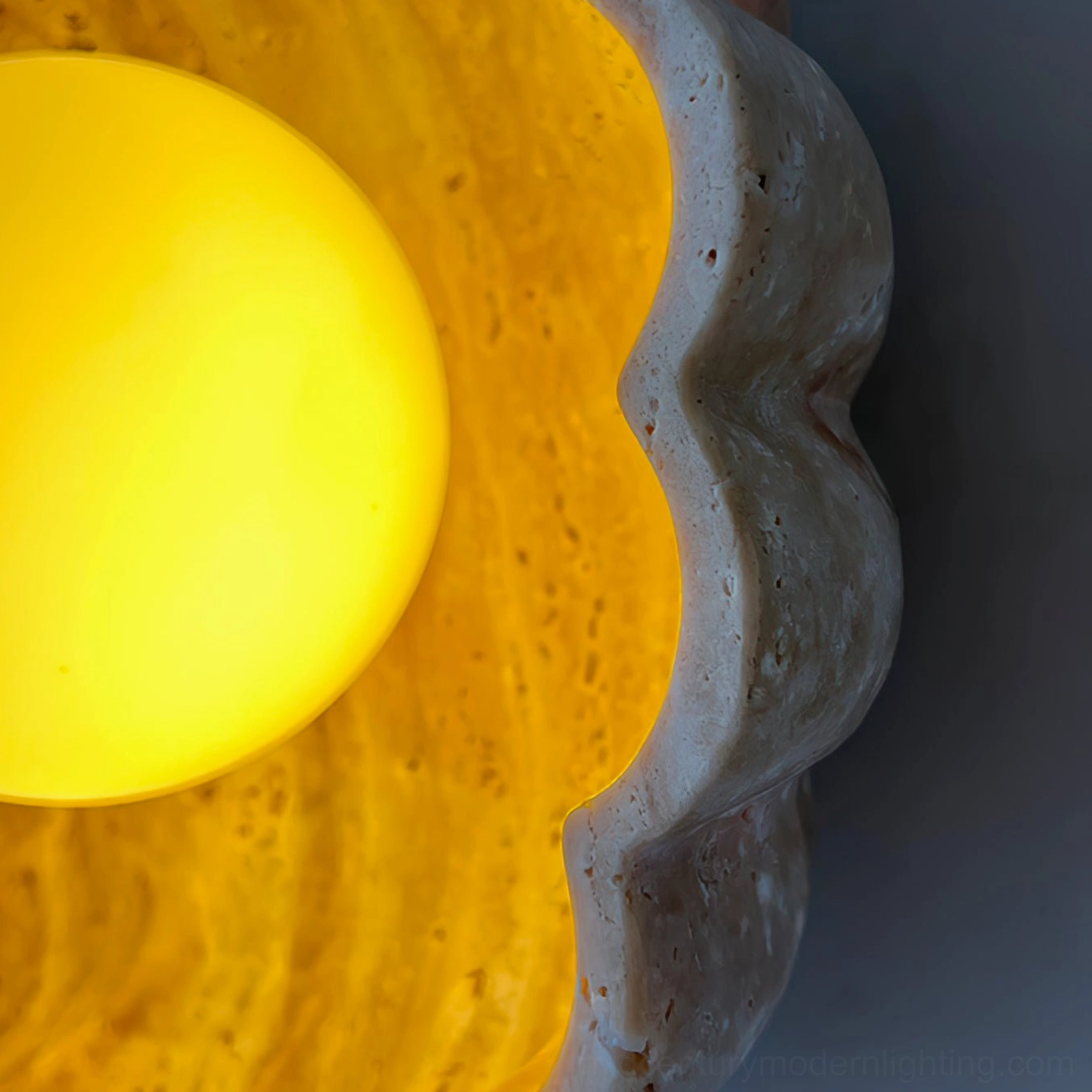 Close-up low-angle view of illuminated scallop wall lamp showing bright interior light and travertine exterior
