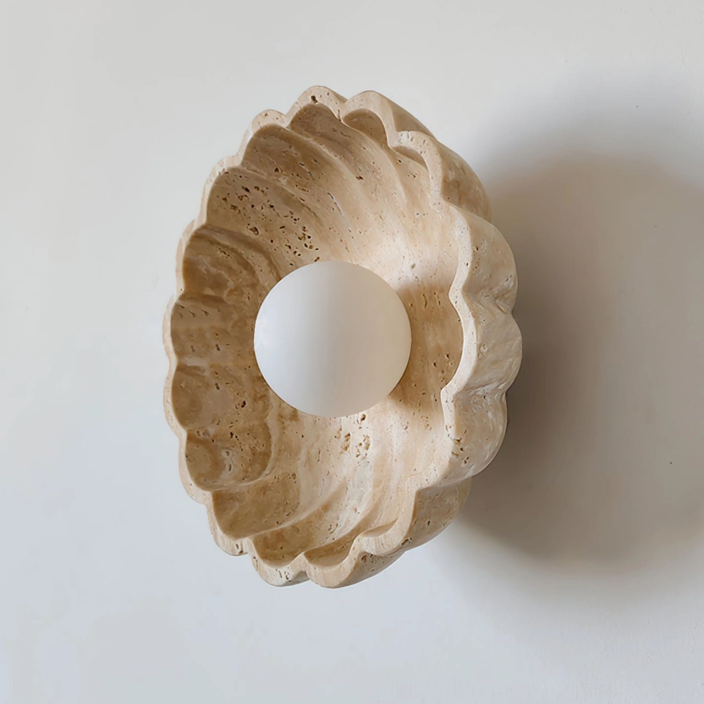 Oval scalloped travertine wall lamp with installed frosted glass bulb, three-quarter angle