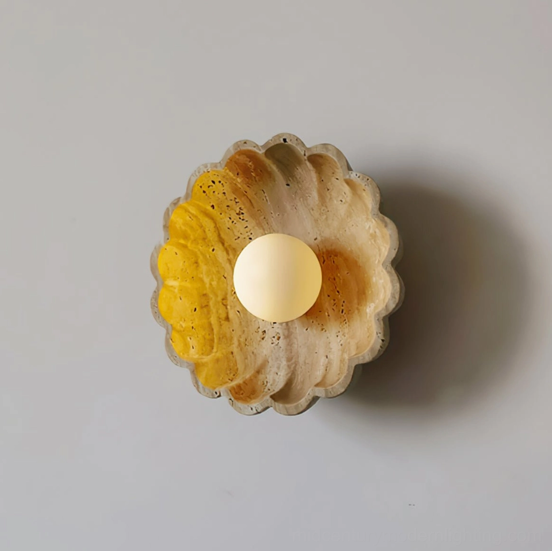 Scallop wall lamp with yellowish travertine finish and tinted bulb side angle view