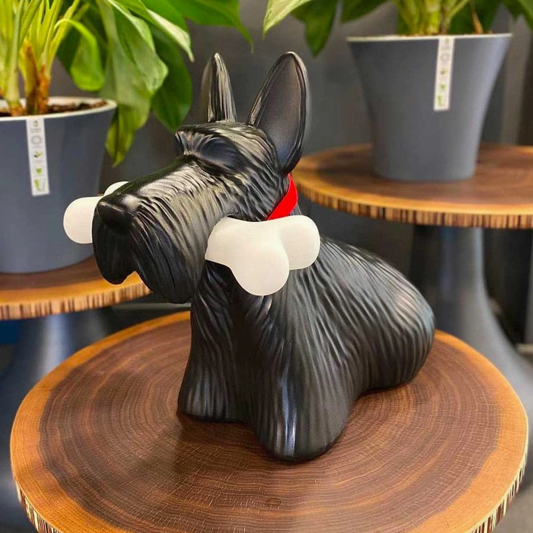 Modern Scottie dog table lamp in black with red collar, three-quarter view on wooden side table with potted plants