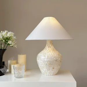Seashell mosaic lamp on white vanity dresser with floral decor and candles, coastal modern bedroom accent lighting