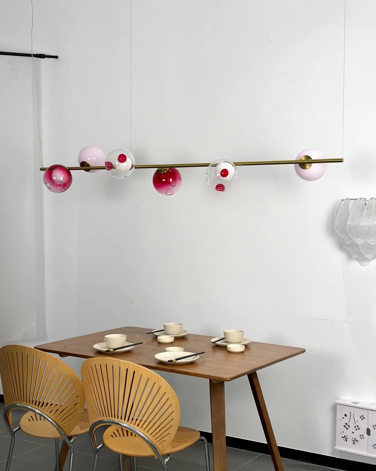 Close-up view of Sedna linear chandelier glass orbs in gold, pink, red, white and clear tones with brass rod support