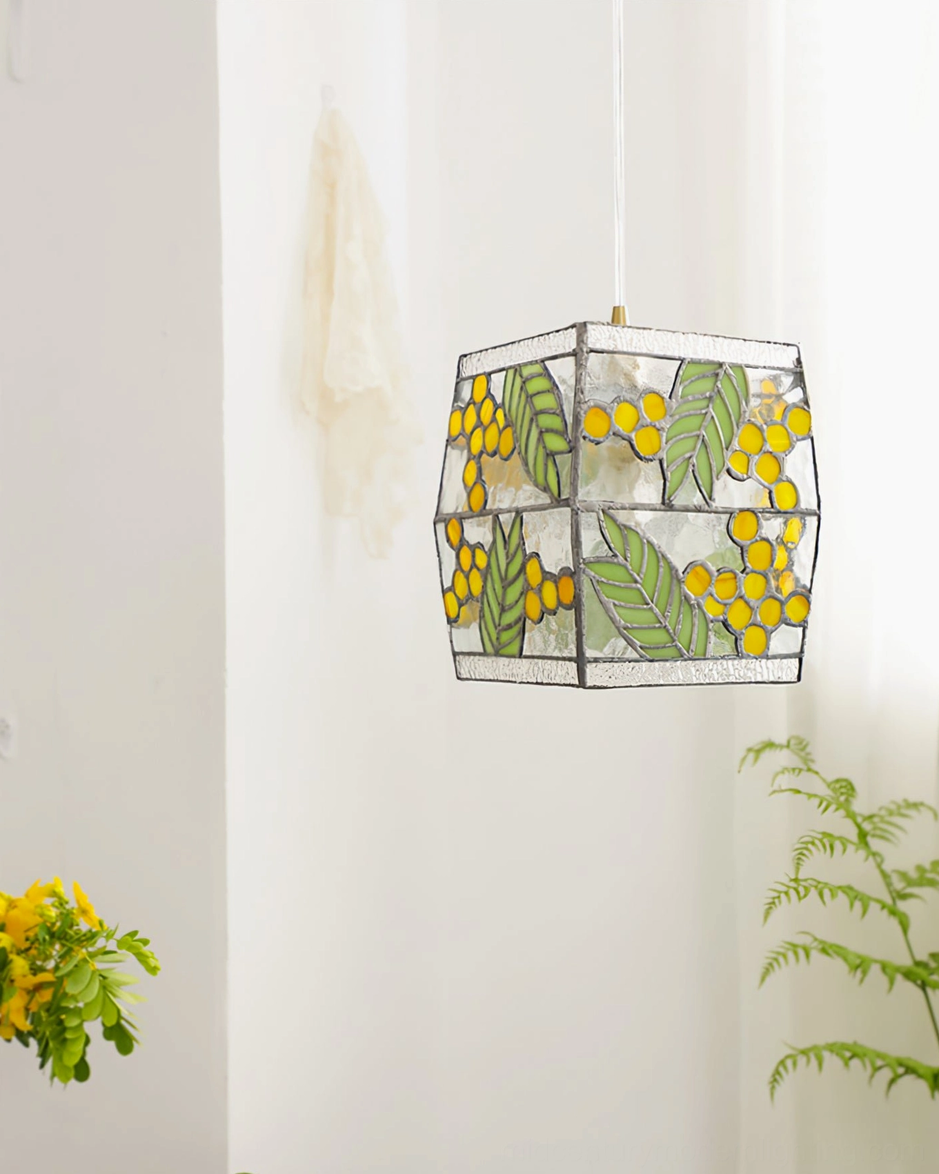 Stained glass cube pendant light with black metal borders and green botanical patterns, hanging in bright indoor space