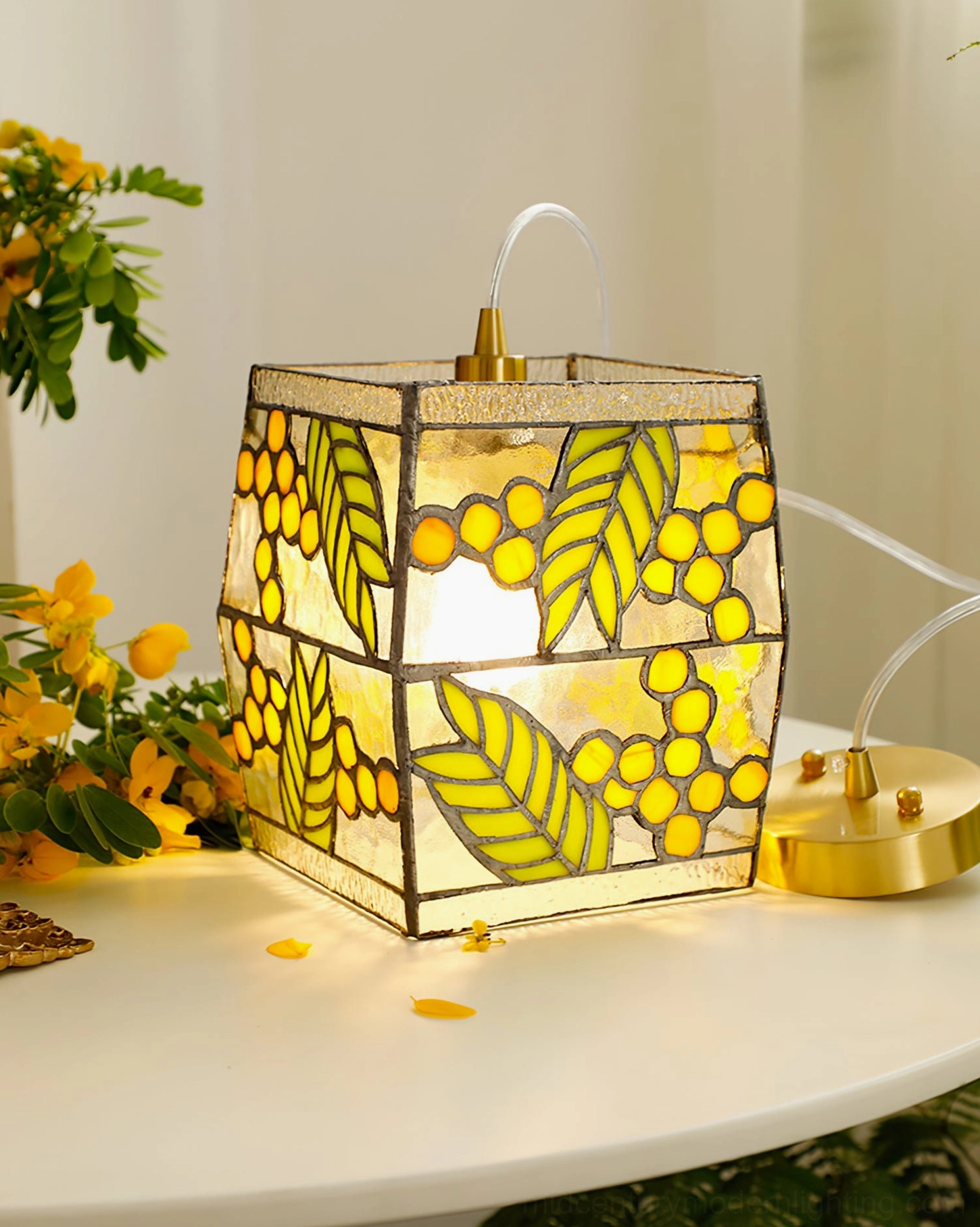 Close-up front view of brass-based seed pendant lamp with glowing warm interior light and detailed stained glass artwork on decorative table