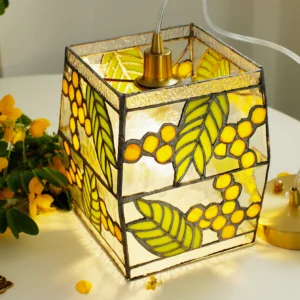 Close-up side view of Seed Pendant Lamp stained glass panels with warm interior light, brass metal fixture and yellow botanical details