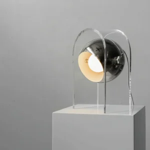 Modern acrylic desk lamp with polished chrome metal base, angled front view on display pedestal