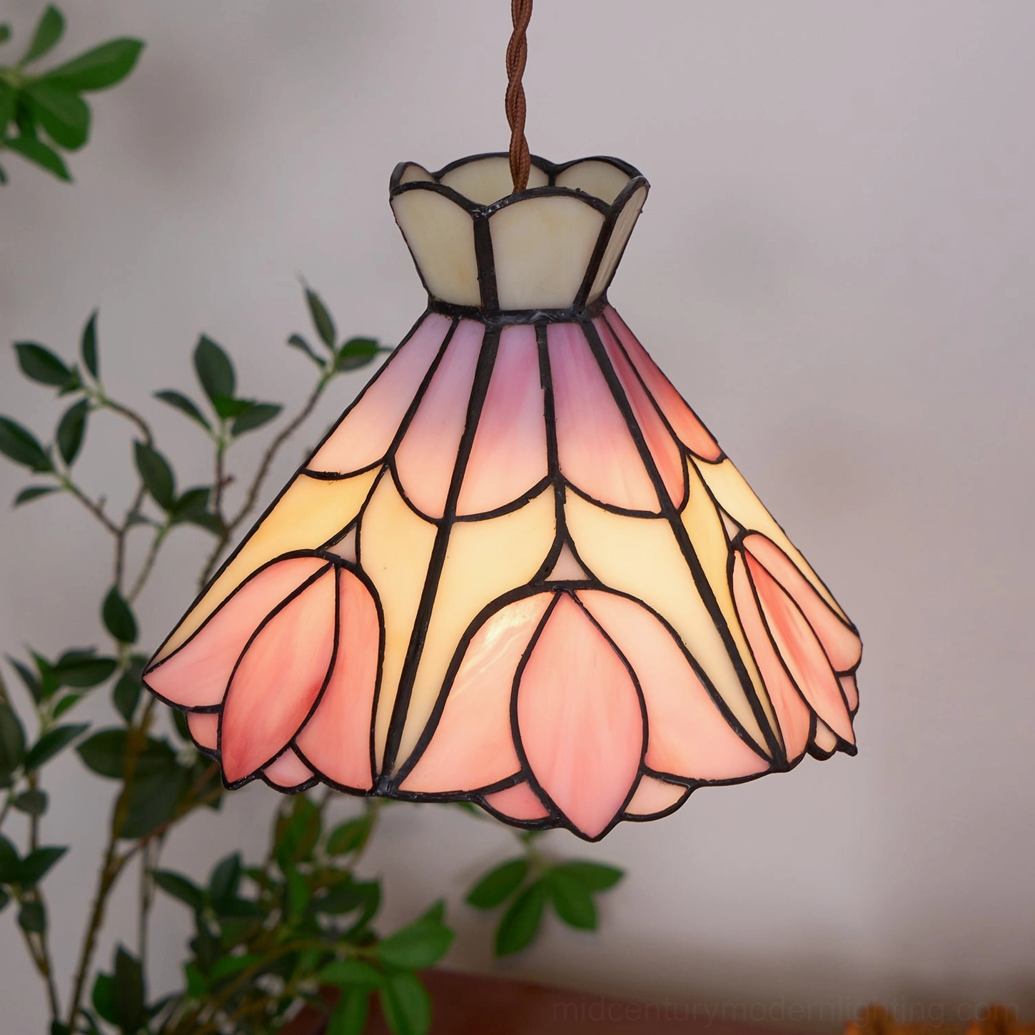 Bright Serena Tiffany pendant light close-up showing warm gradient pink-yellow stained glass in home corner with greenery