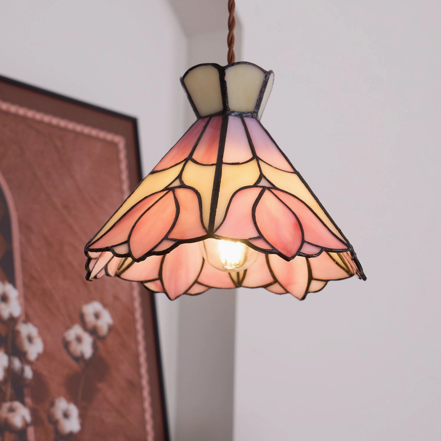 Lit vintage Serena pendant lamp with exposed Edison bulb and pink glass petals in home interior with floral wall art