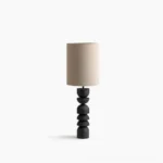Sergio sculptural table lamp with stacked blackened wood base and beige linen shade on white background