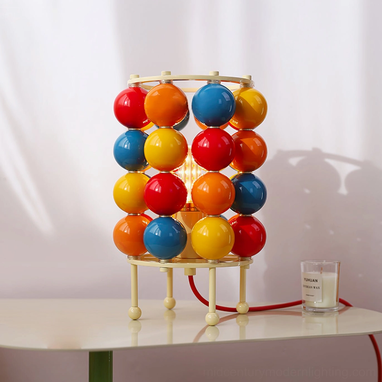 Modern Sfera ball table lamp on white side table with red power cord and decorative candle