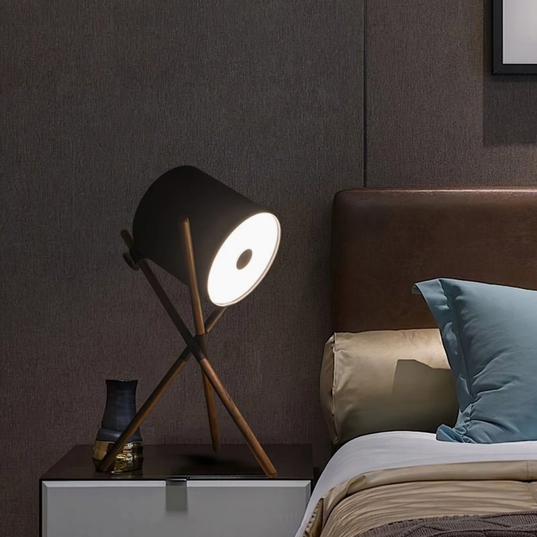 Black and dark wood tripod table lamp with matte black shade creating ambient lighting on bedroom bedside table