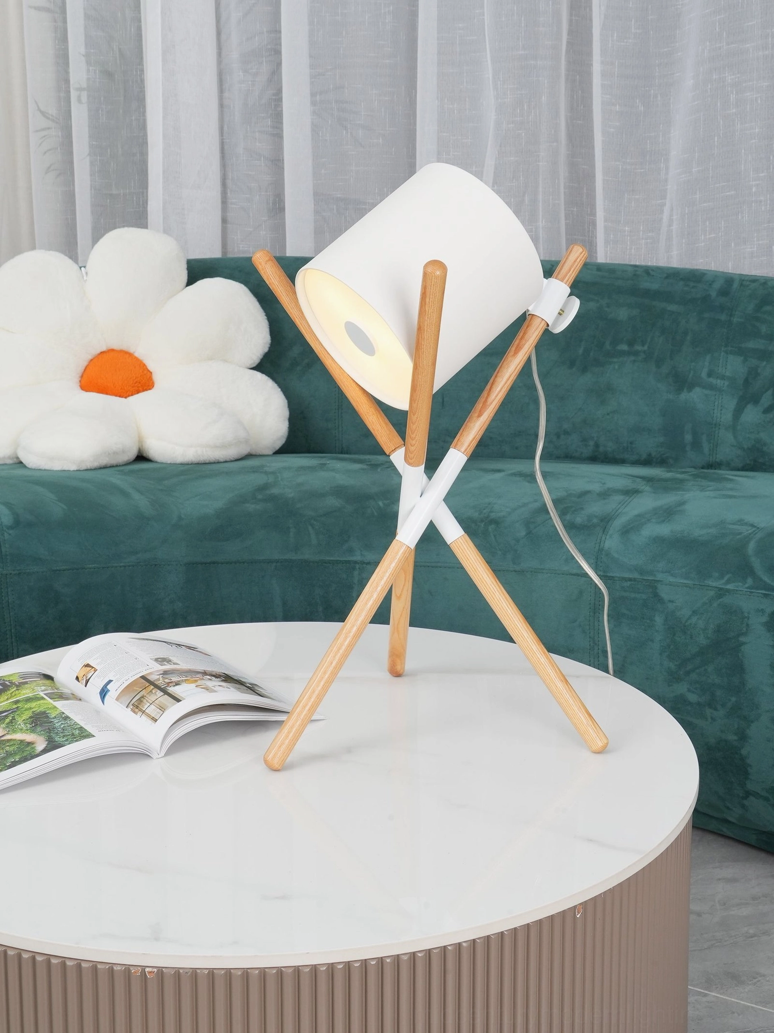 Natural wood tripod table lamp with illuminated white shade in cozy minimalist living room interior