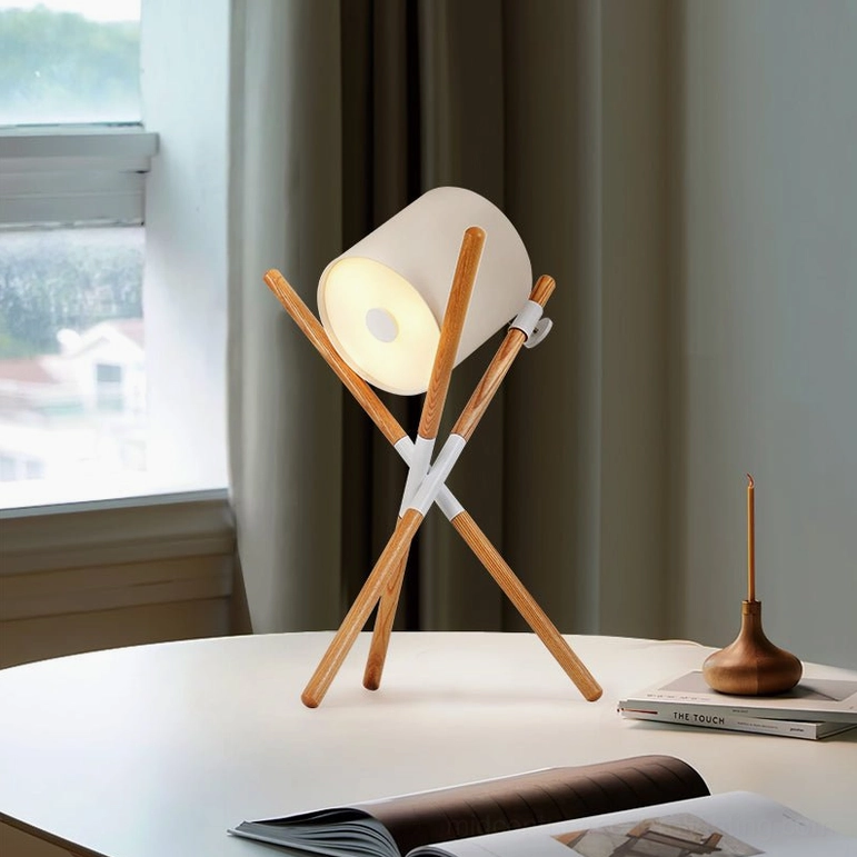 Natural wood tripod table lamp with white fabric shade on home table by window with decorative accessories