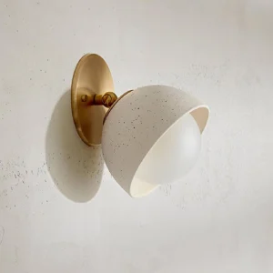 Natural travertine stone wall sconce mounted on textured concrete wall - three-quarter angle view displaying unique stone veining and texture
