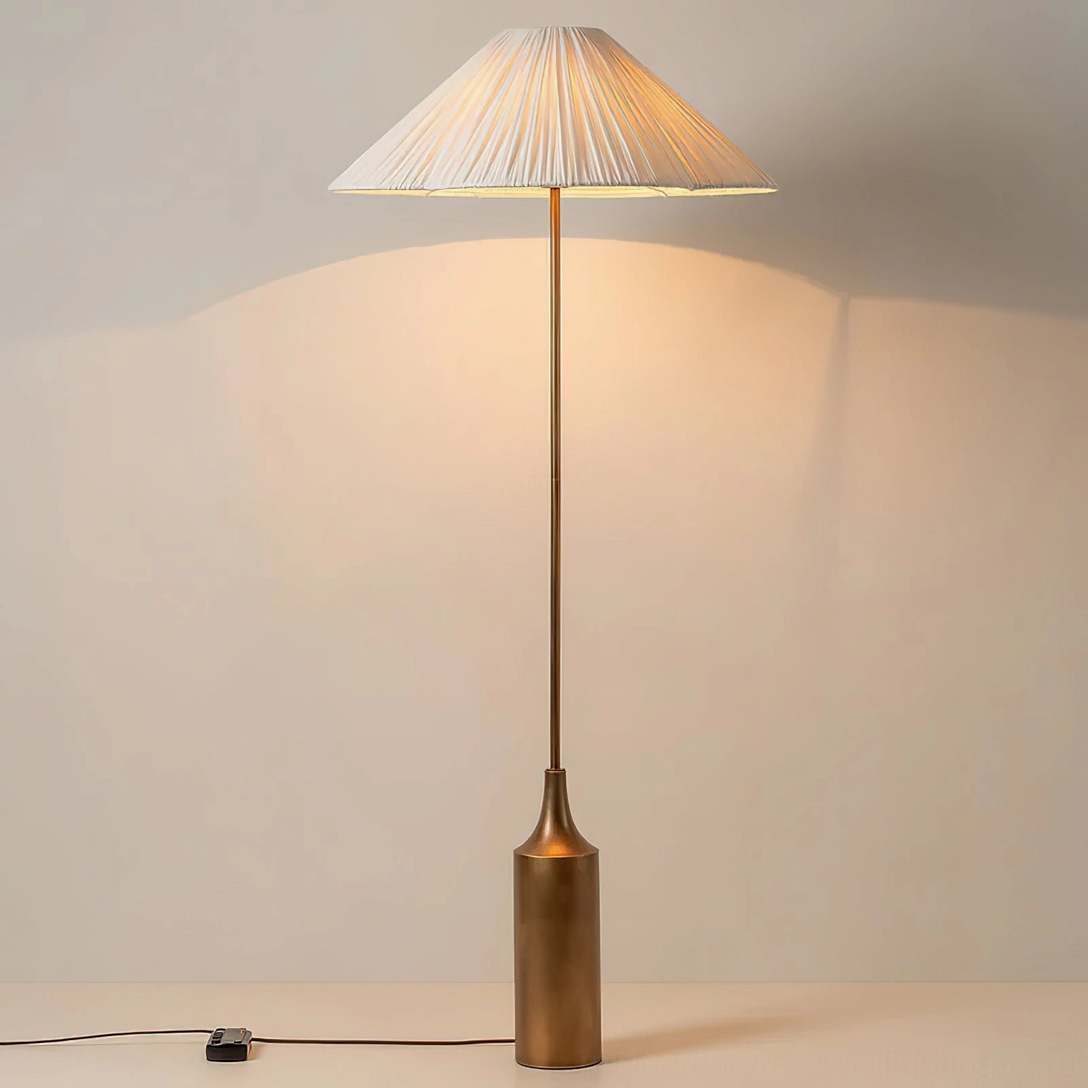 Sierra floor lamp illuminated at night, right side view, showing warm ambient light diffusion through the pleated linen shade and bronze metal base