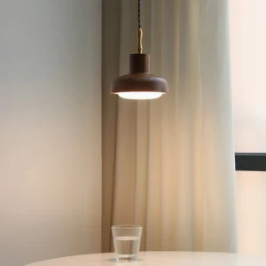 Silas pendant light glowing warm amber in mid-century modern dining corner, suspended above table with sheer curtains and neutral interior