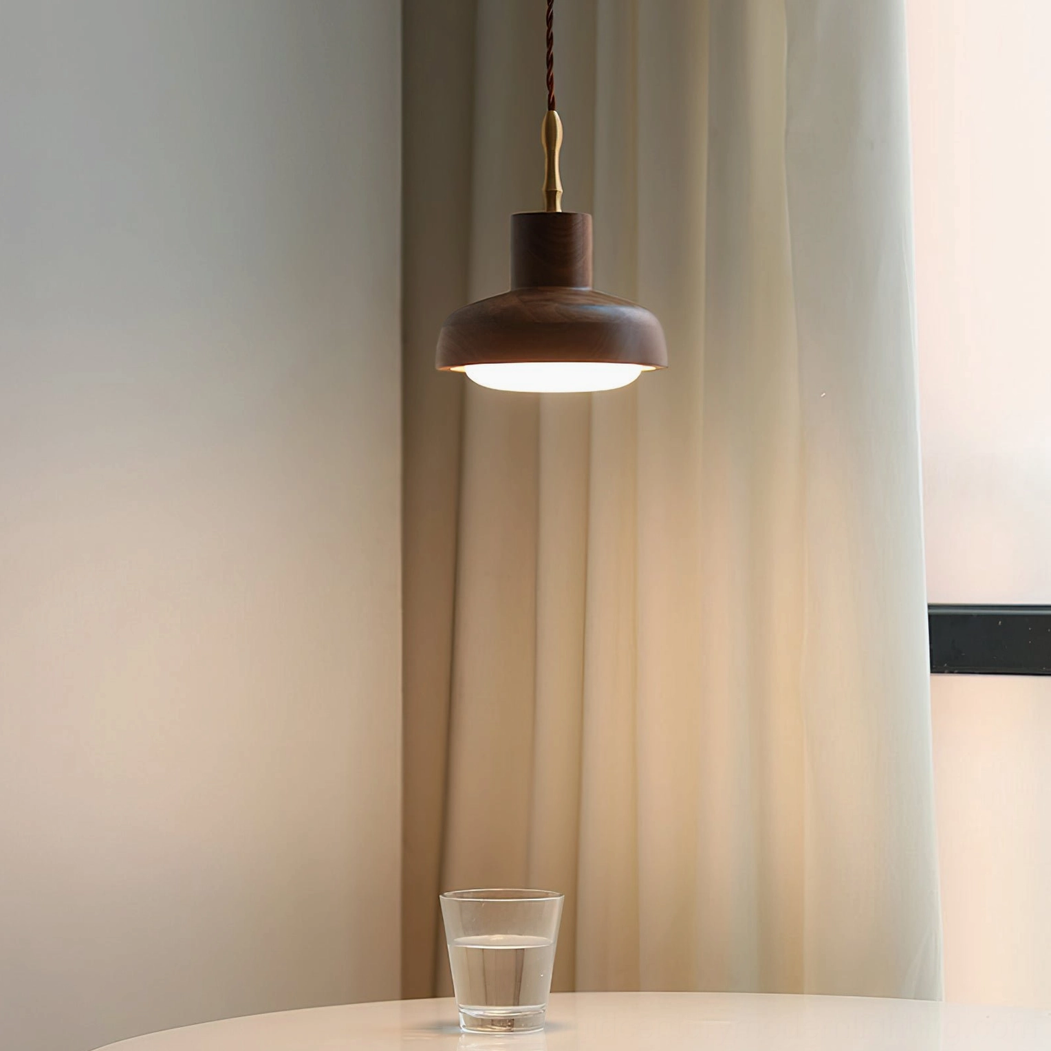 Silas pendant light glowing warm amber in mid-century modern dining corner, suspended above table with sheer curtains and neutral interior