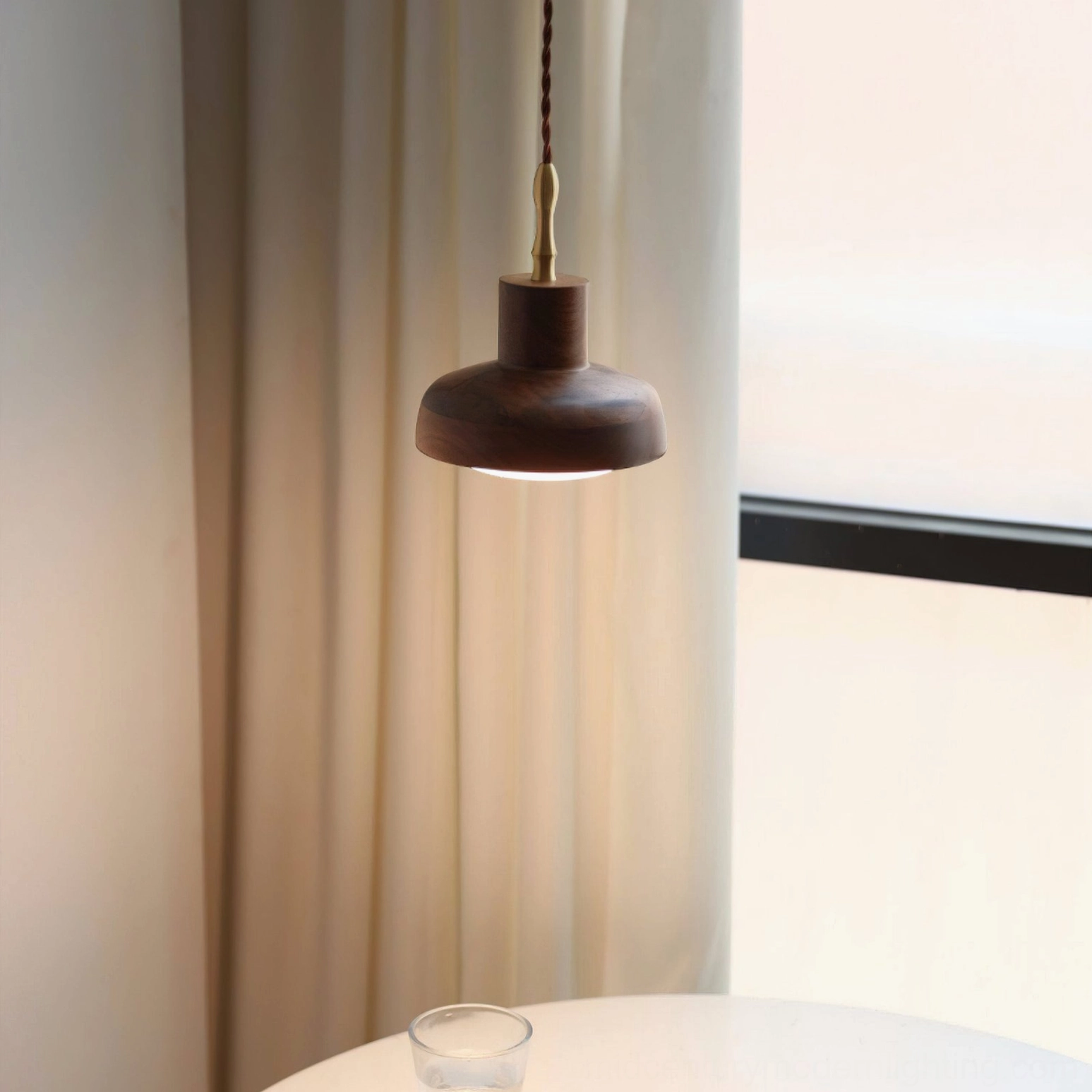 Walnut pendant light illuminating side dining area near window, glass cup on round table, japandi minimalist interior style