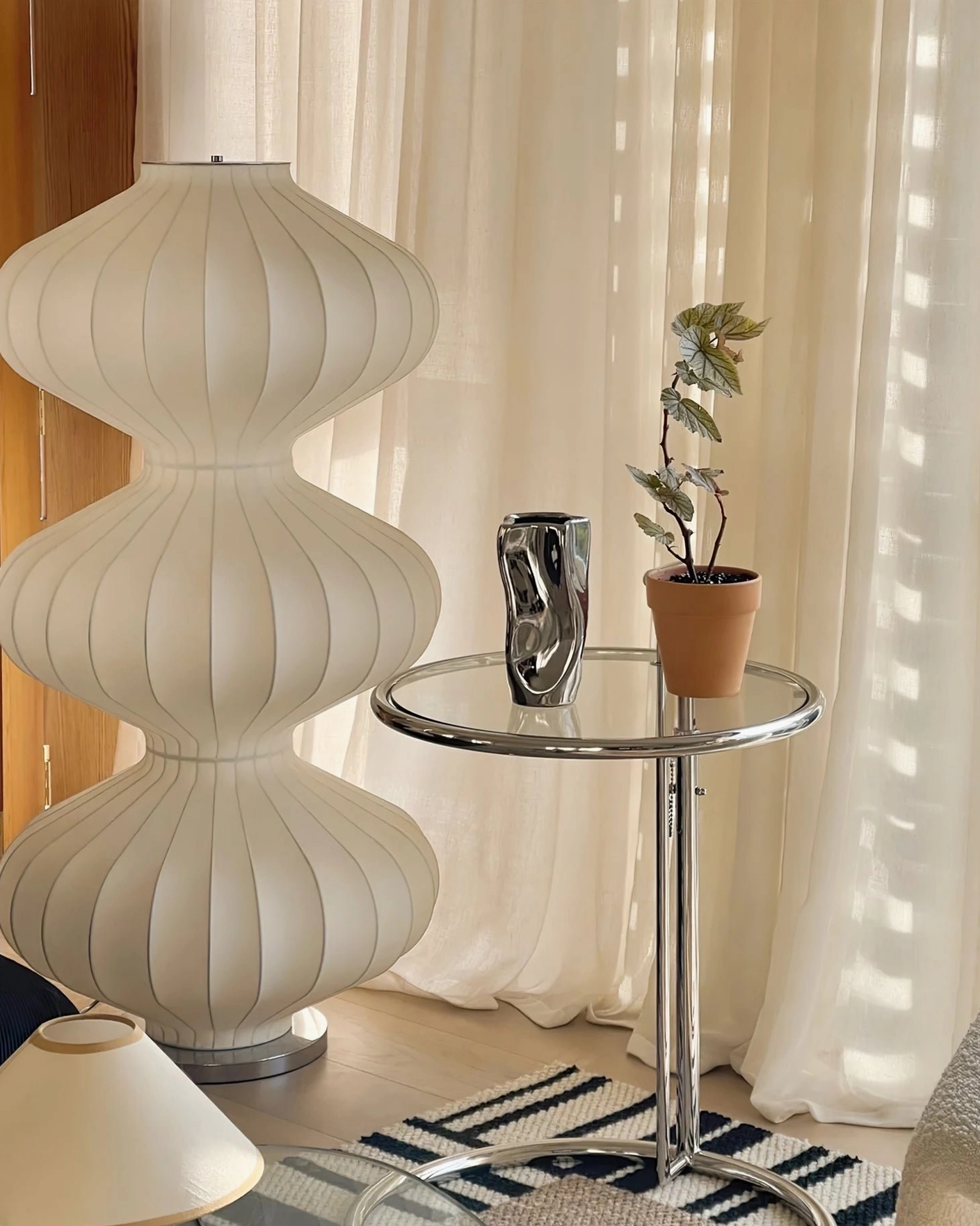 Tall white silk gourd floor lamp eye-level side view next to metallic side table in sunlit modern nook