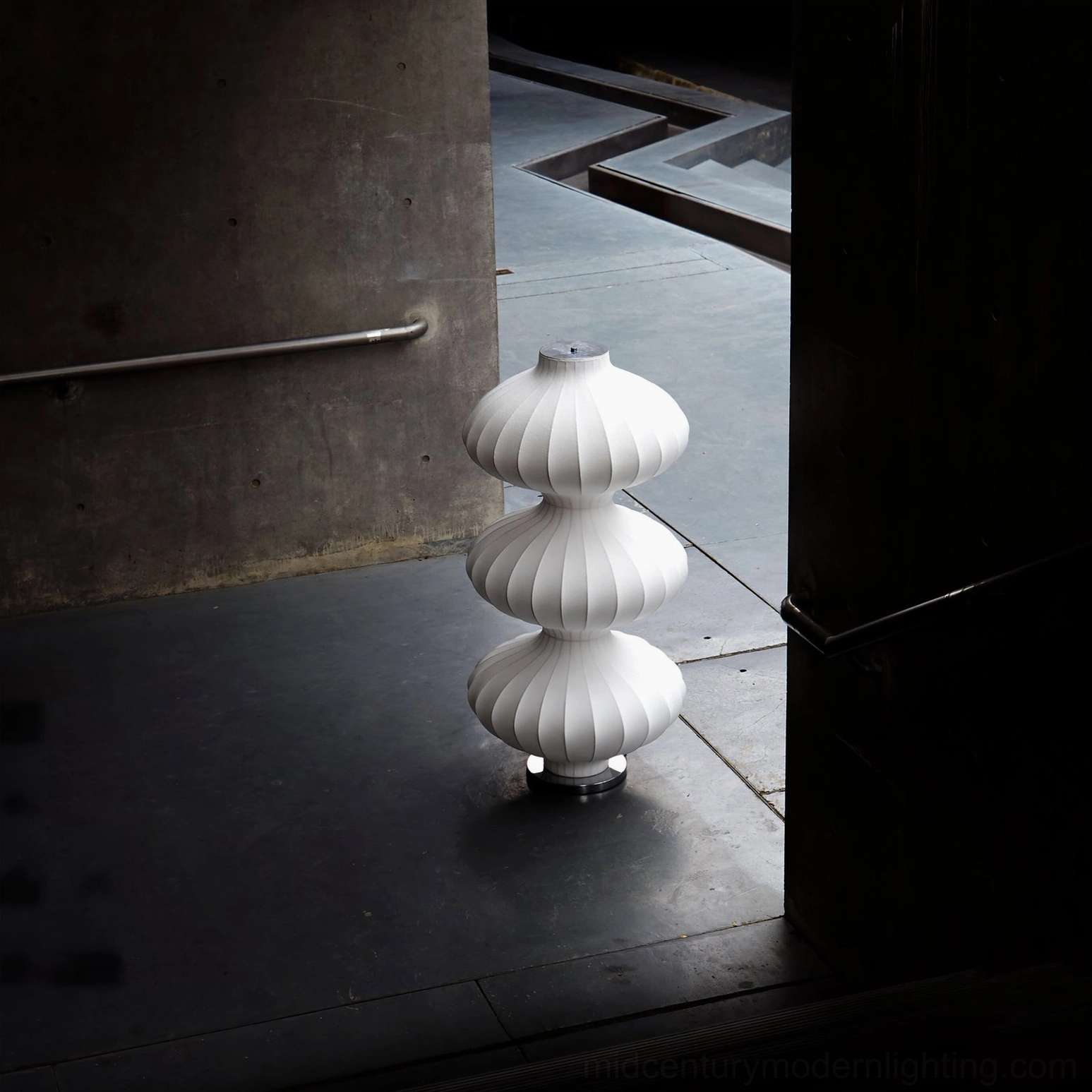 Tall white silk gourd floor lamp side view in concrete corridor, vertical ribbed texture visible