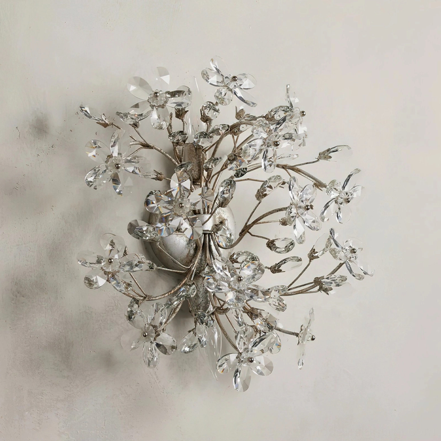 Silver metal frame crystal flower wall sconce, frontal view showing delicate botanical crystal cluster design on textured wall