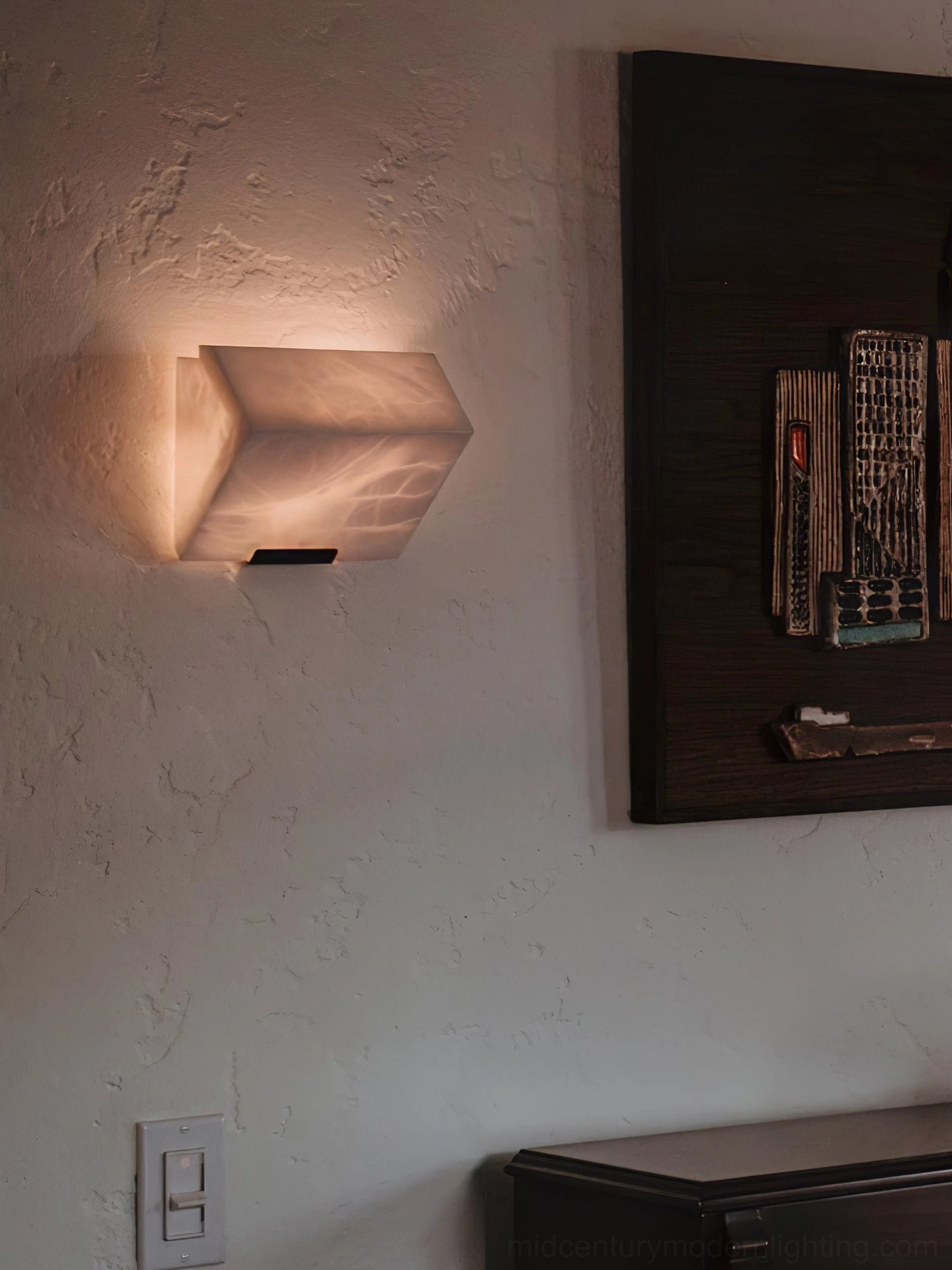 Single-light alabaster wall sconce against textured accent wall with wall art, modern rustic minimalist design