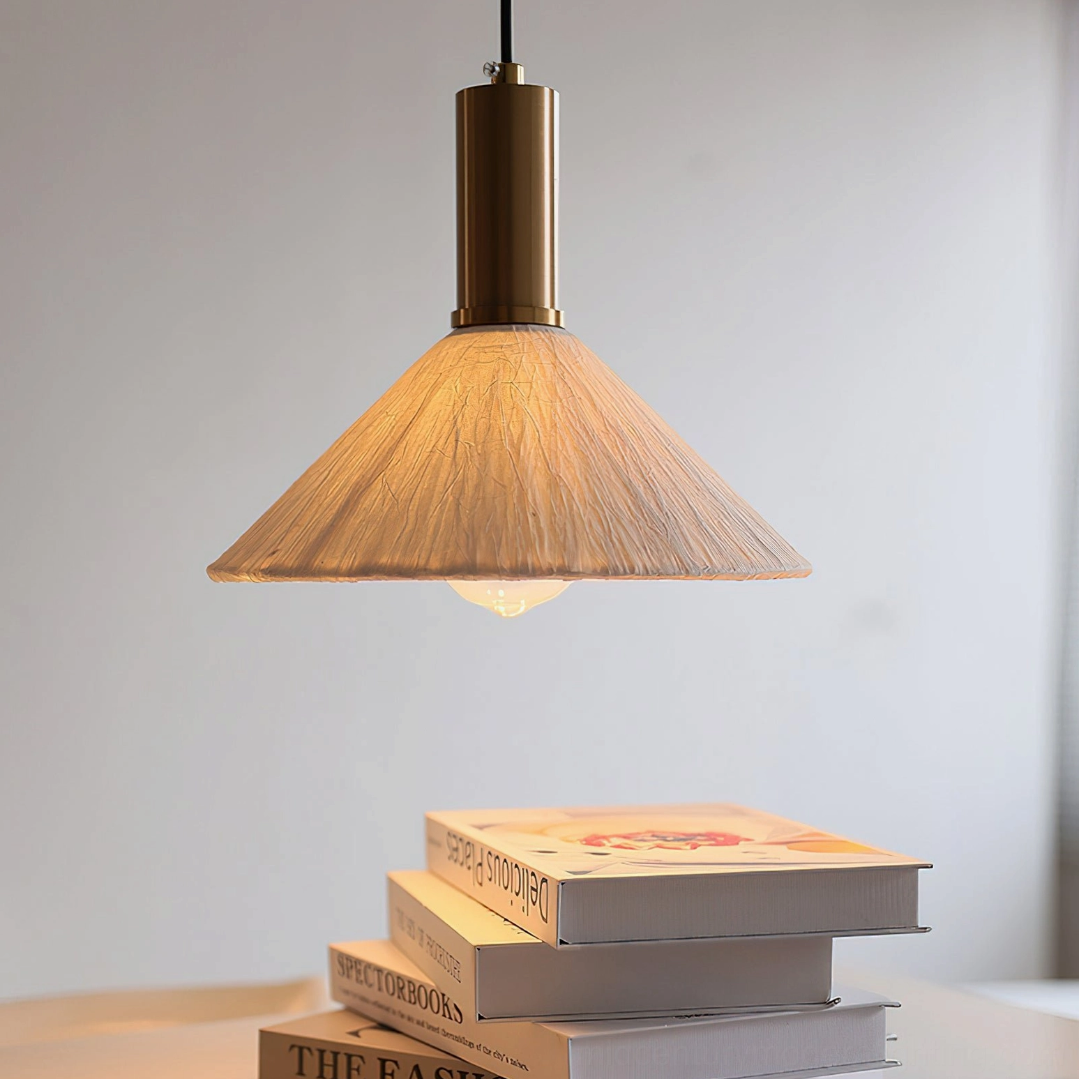 Bottom-up view of Siya pendant light illuminating over stacked art books, warm textured paper shade bohemian aesthetic