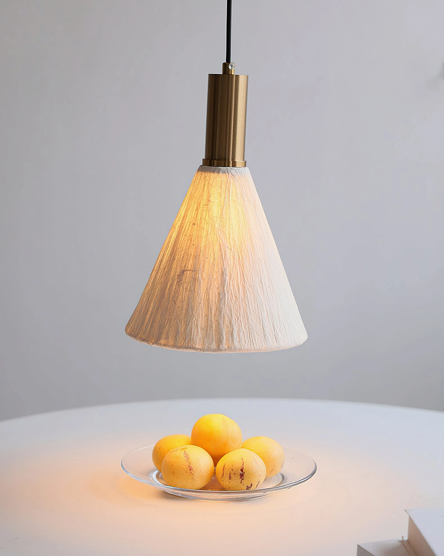 Tapered cone Siya pendant light with off-white textured fabric shade over round dining table with fruit platter